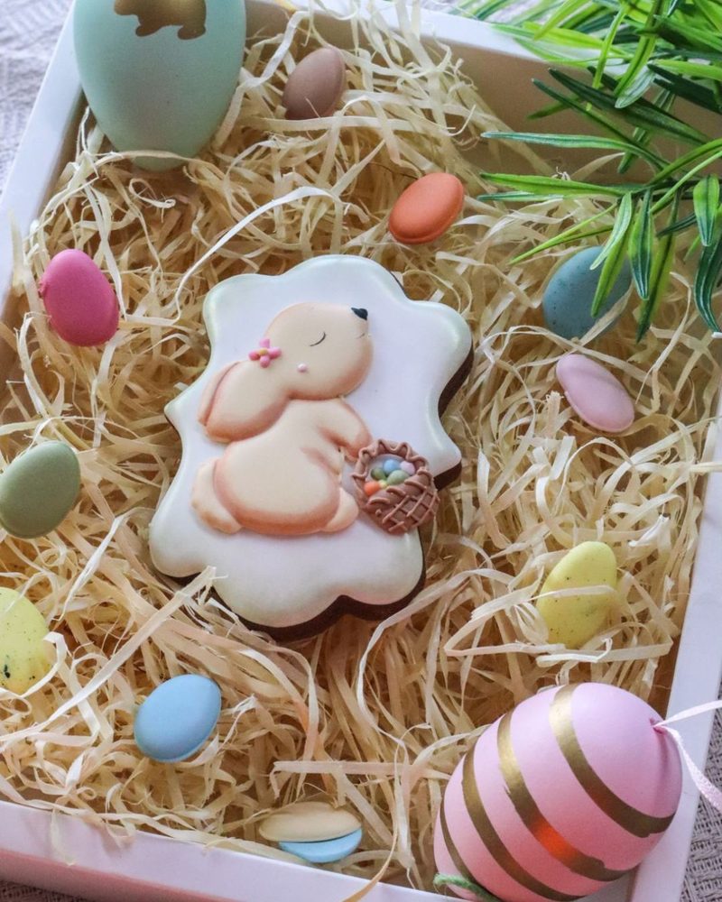 Biscoito de coelhinha com cesta de miniovos, apoiado em caixa com ovinhos